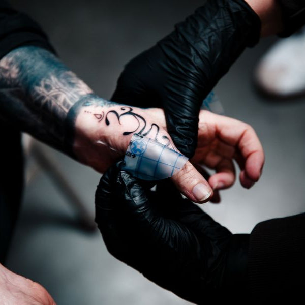 Two people with tattoos on their hands holding fingers together against a dark background